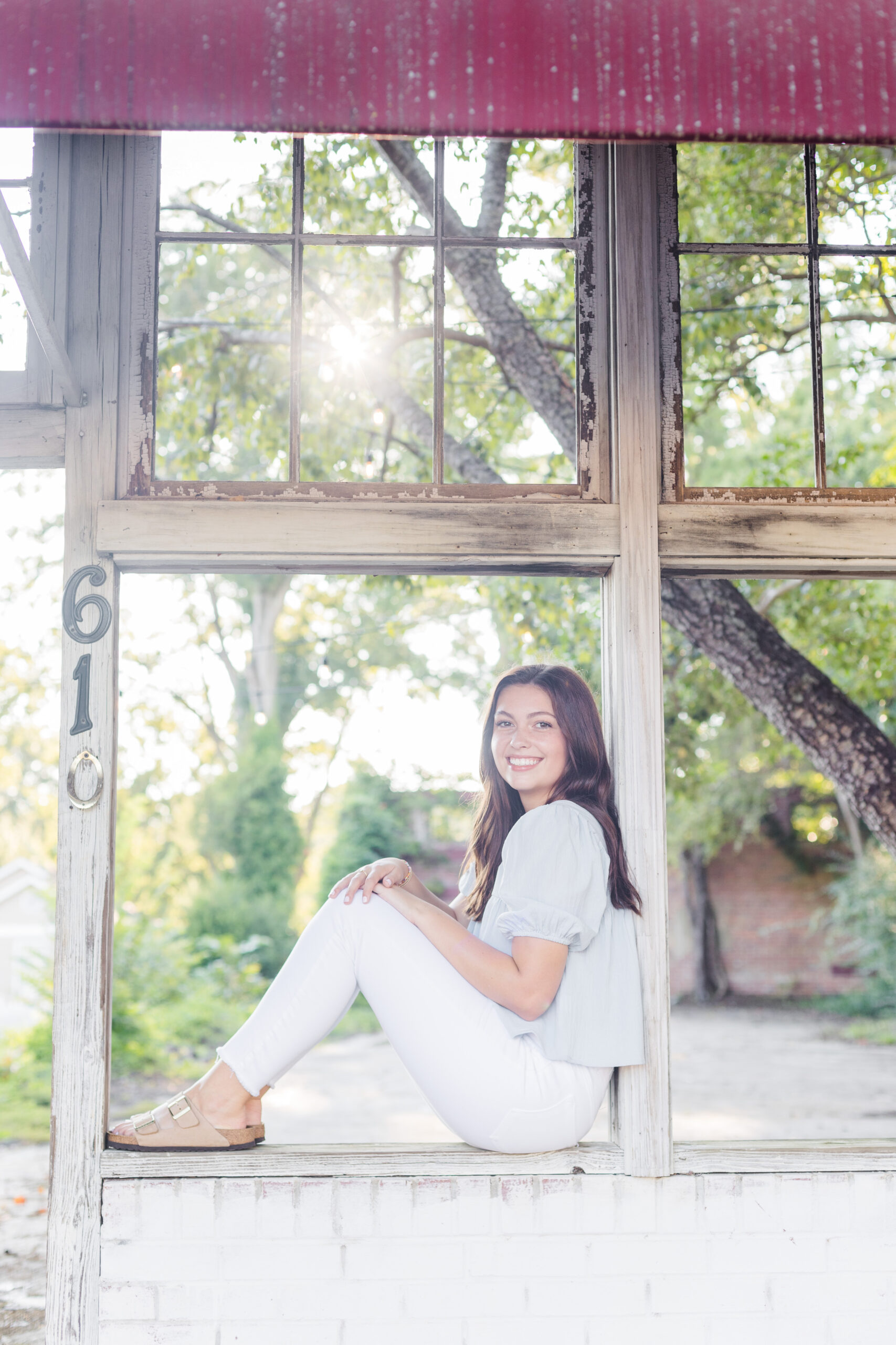 High school senior girl sitting in a window of abandoned building for senior portraits