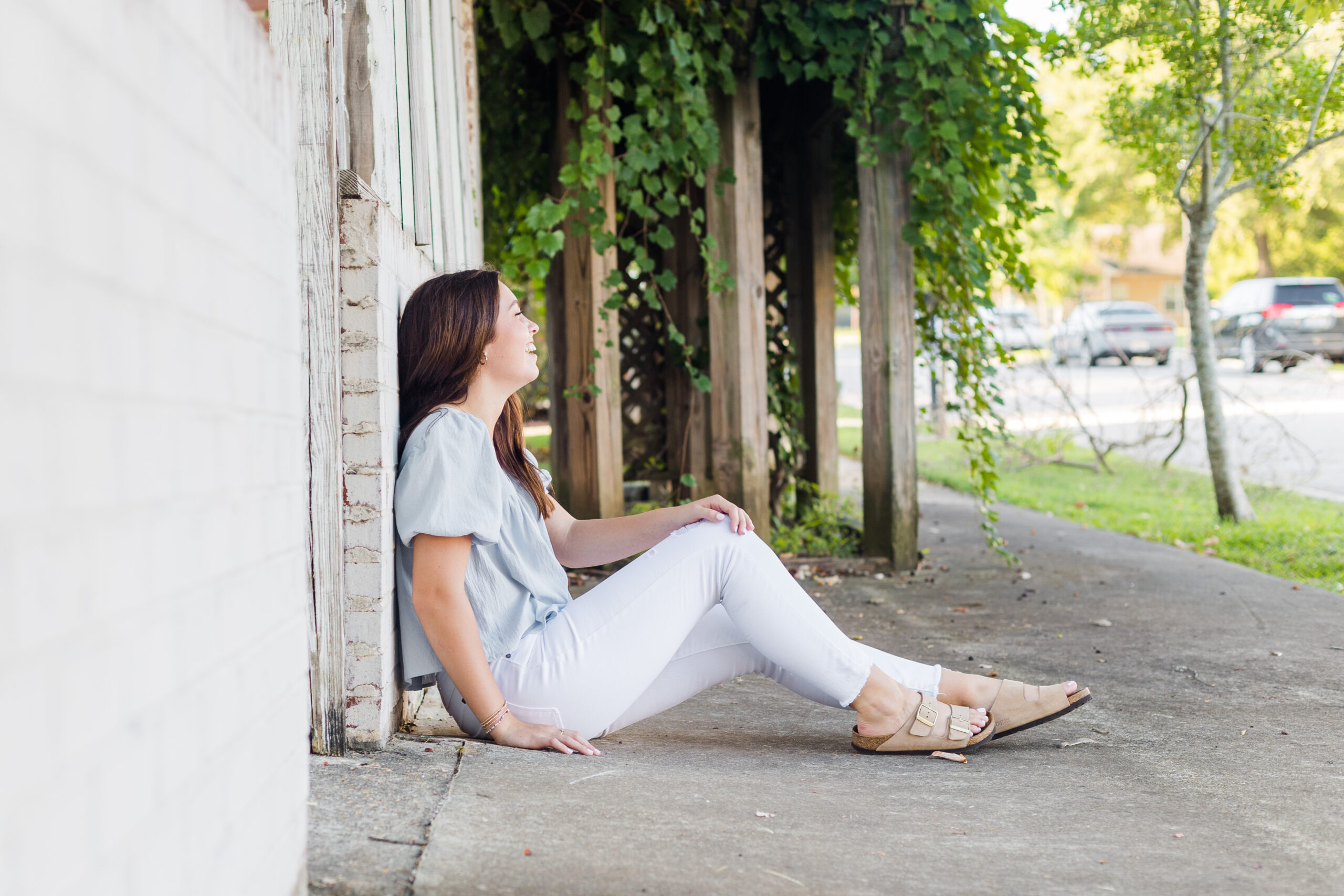 High school senior laughing while sitting on the sidewalk for senior portraits