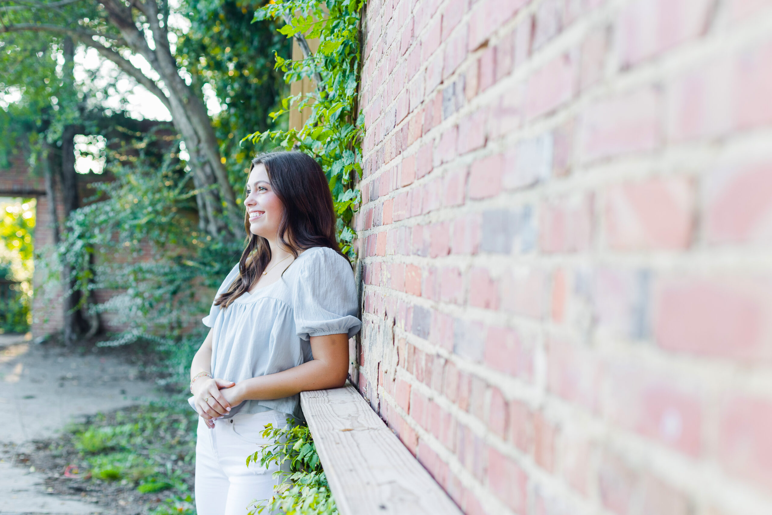 High school girl posing for senior portraits next to a brick wall