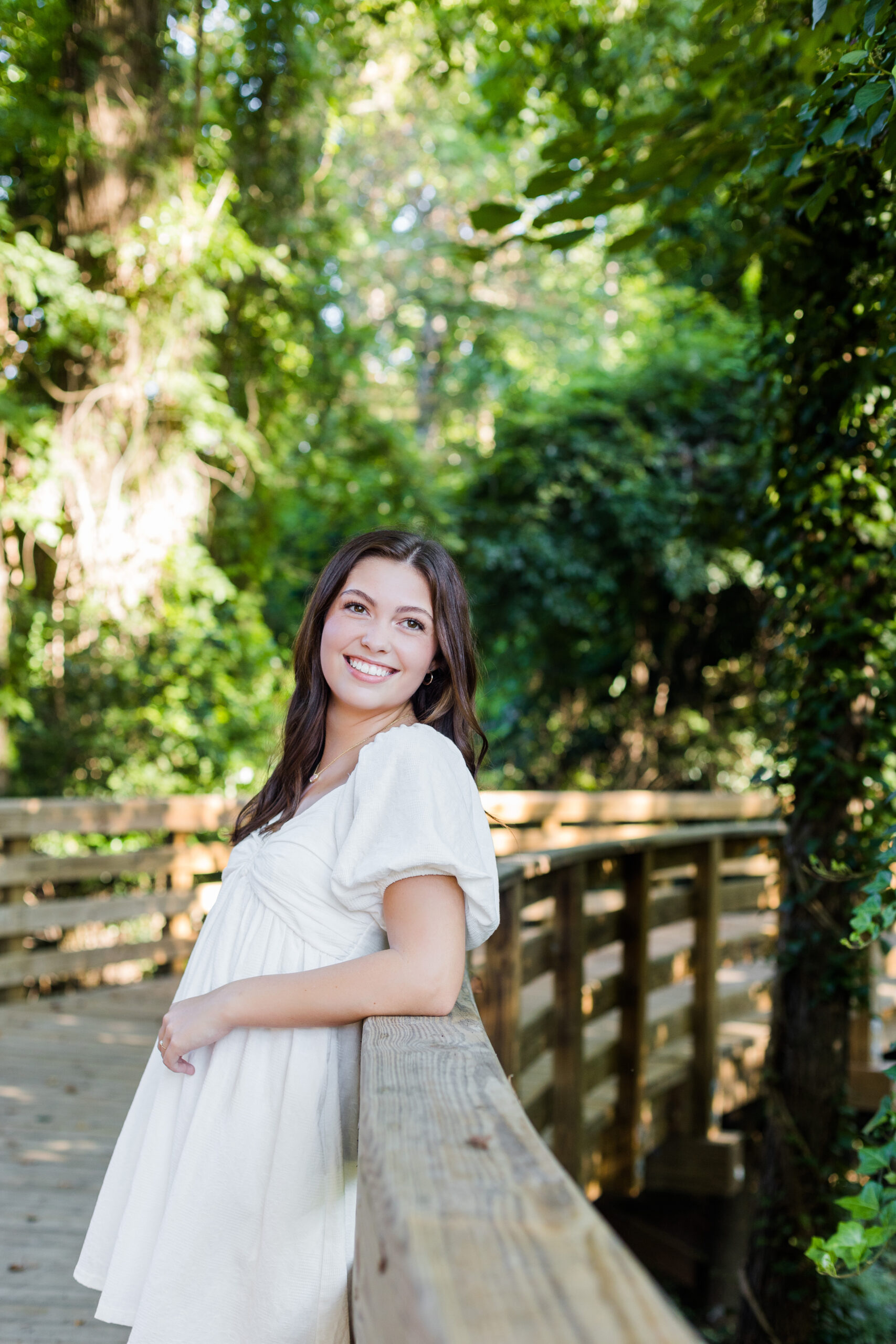 High school senior girl leaning against a wooden bridge railing